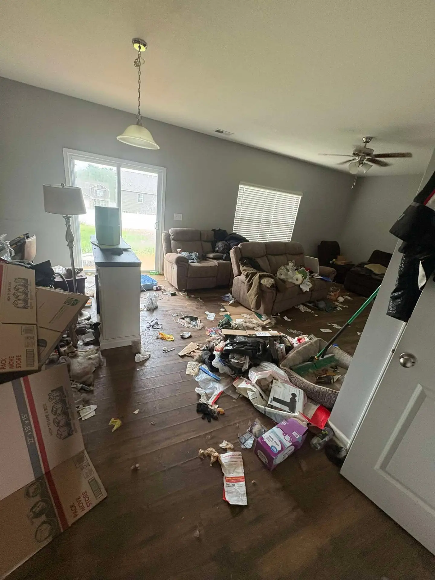 Before cleaning: living room with moving boxes, trash and scattered belongings across the hardwood floor