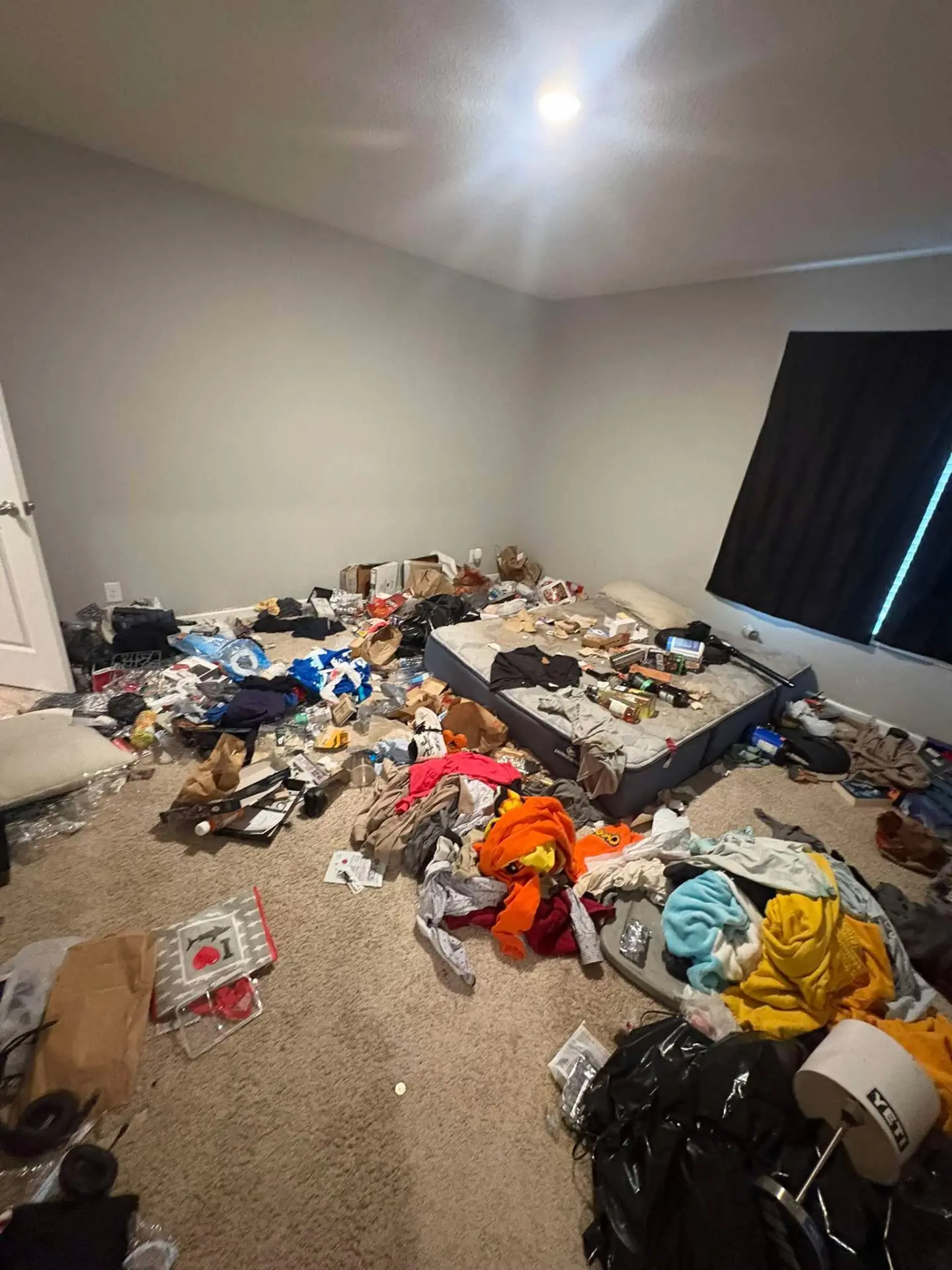 Before cleaning: bedroom with clothing, trash and belongings covering the carpet and mattress