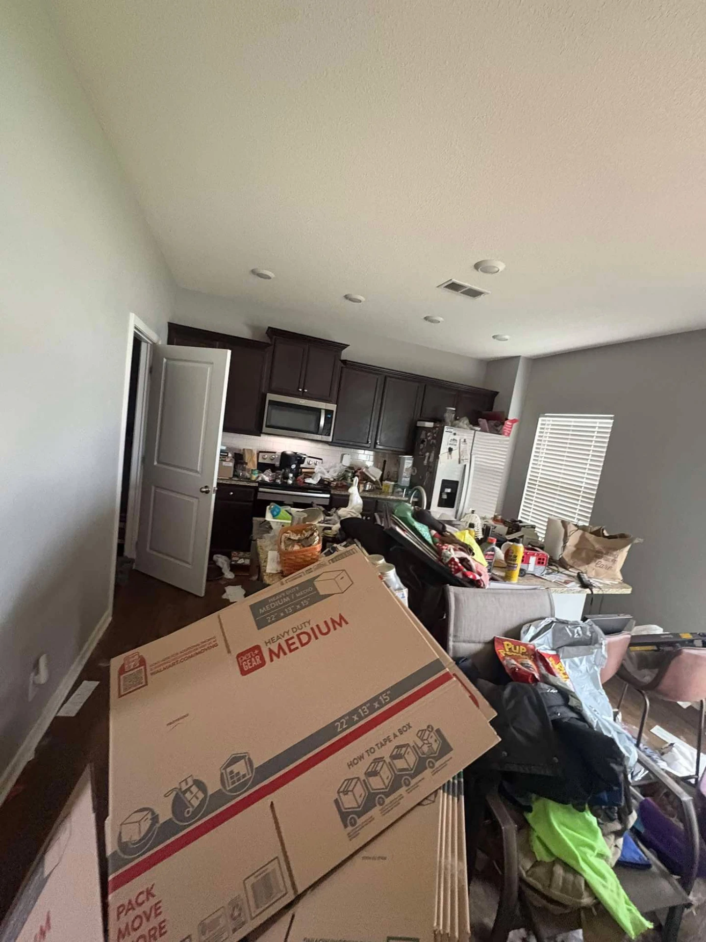 Before cleaning: kitchen and dining area buried in moving boxes, bags and cluttered countertops